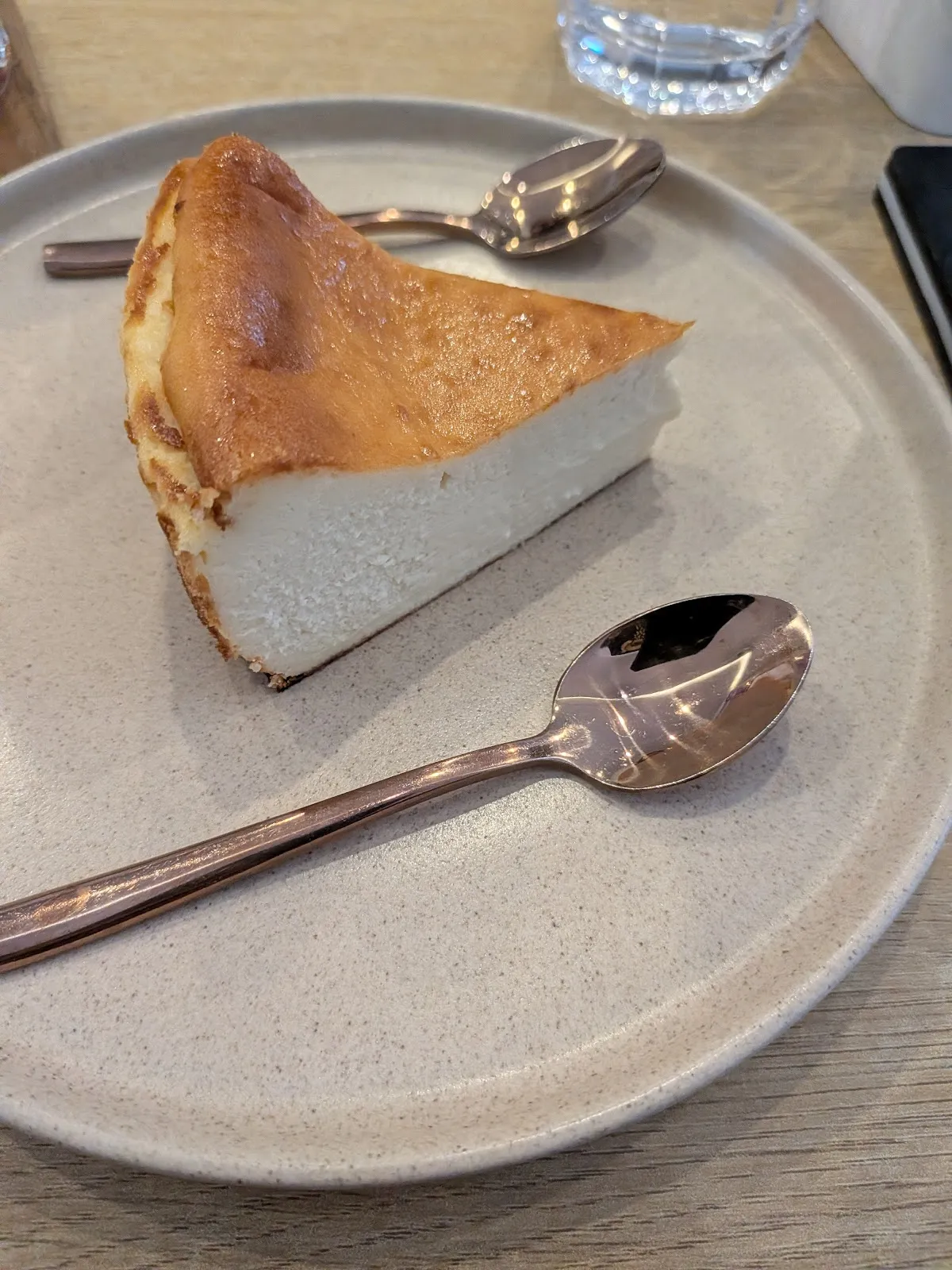 Slice of matcha cheesecake on a stoneware plate with a copper spoon