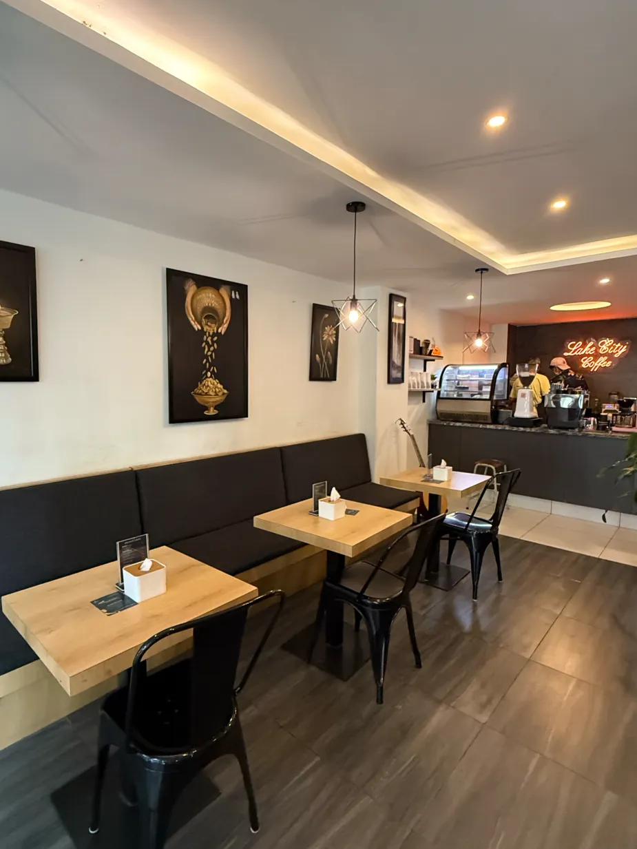 Warm interior of Lake City Cafe with banquette seating, framed coffee artwork, and a glowing neon Lake City Coffee sign over the bar